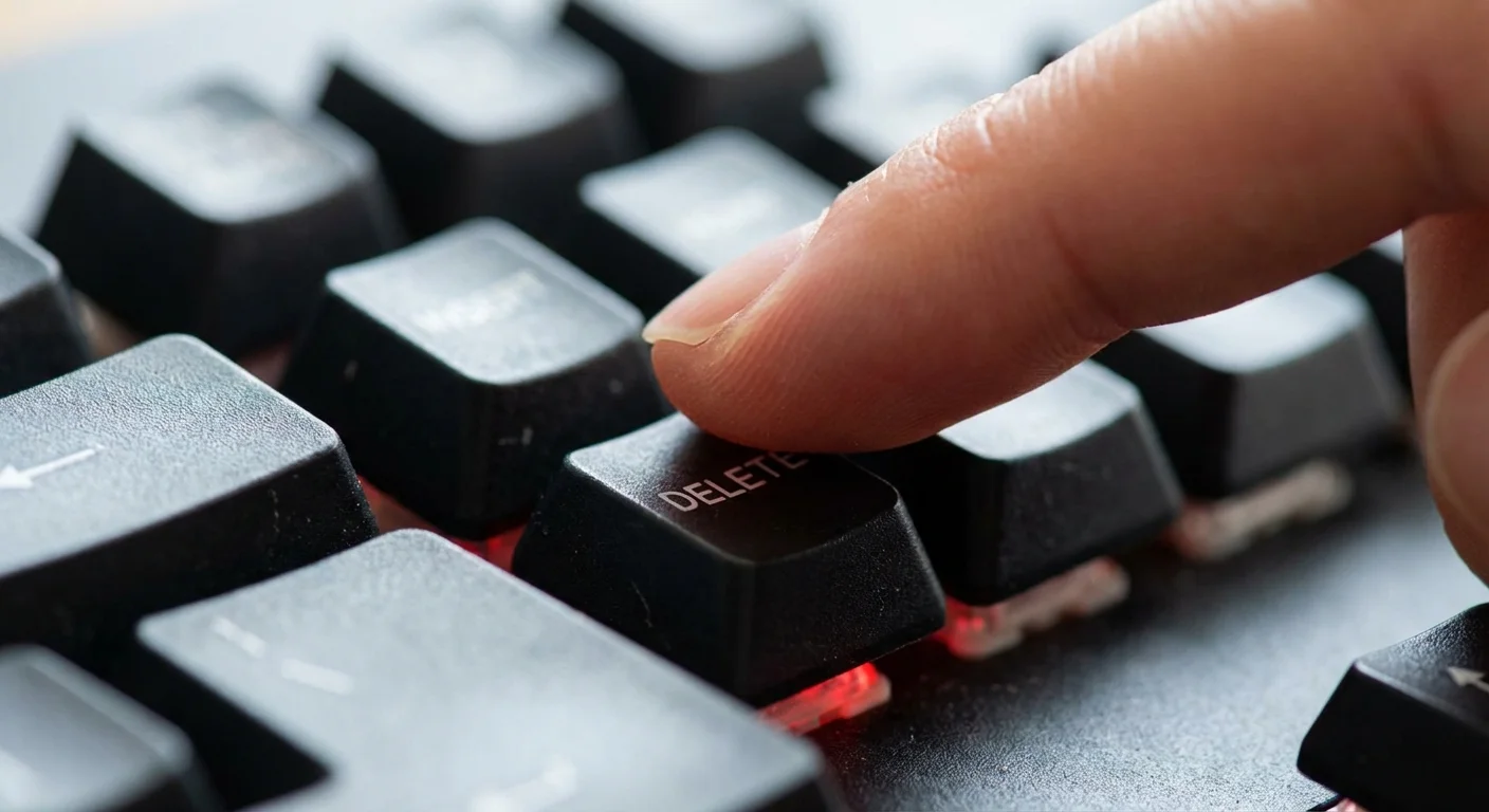 A close-up of a finger about to press the delete key on a computer keyboard.
