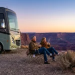 A retired couple sits outside their motorhome at sunrise overlooking a vast desert canyon.