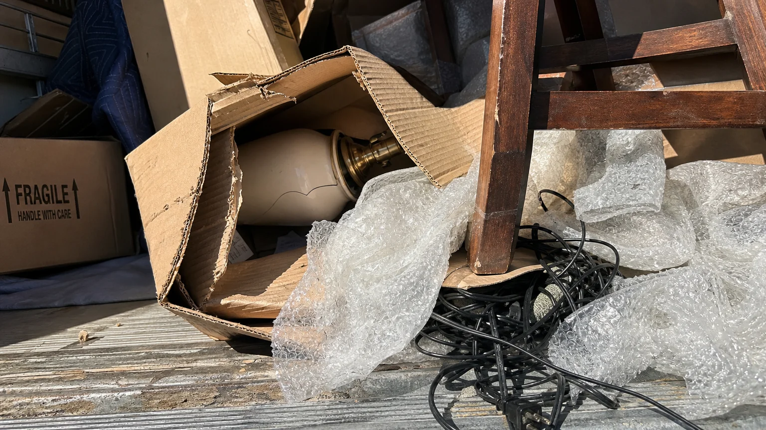 A close-up of a damaged box and a cracked lamp in the back of a moving truck, showing the risks of a physical move.