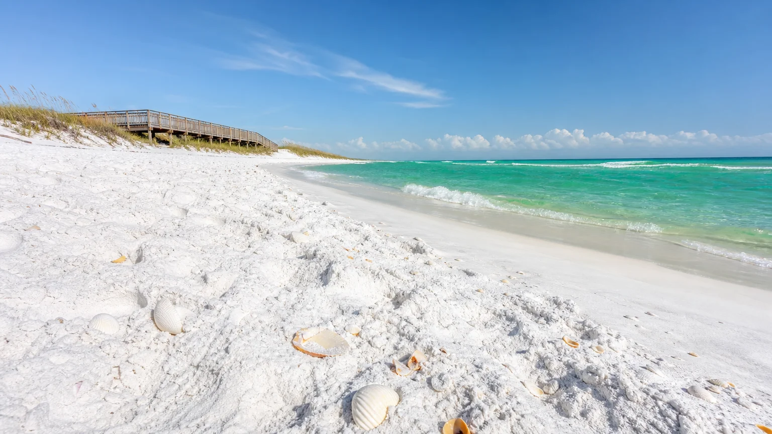 A wide beach view in Gulf Shores, Alabama, showing bright white sand and clear turquoise water under a sunny sky.