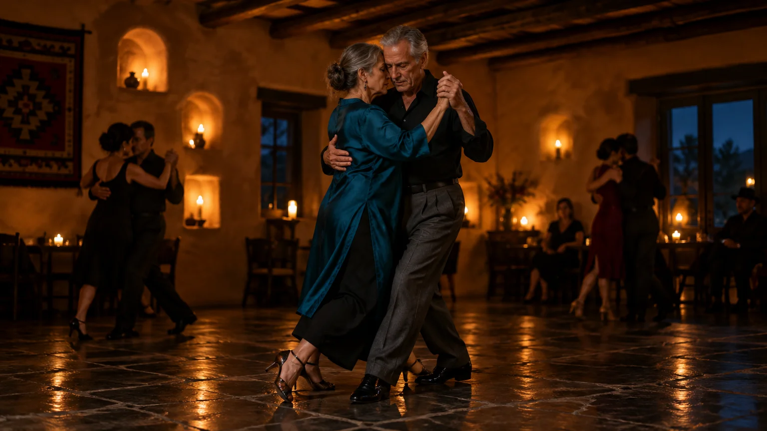 Older couple dancing tango in a candlelit adobe room with other couples dancing in the background.